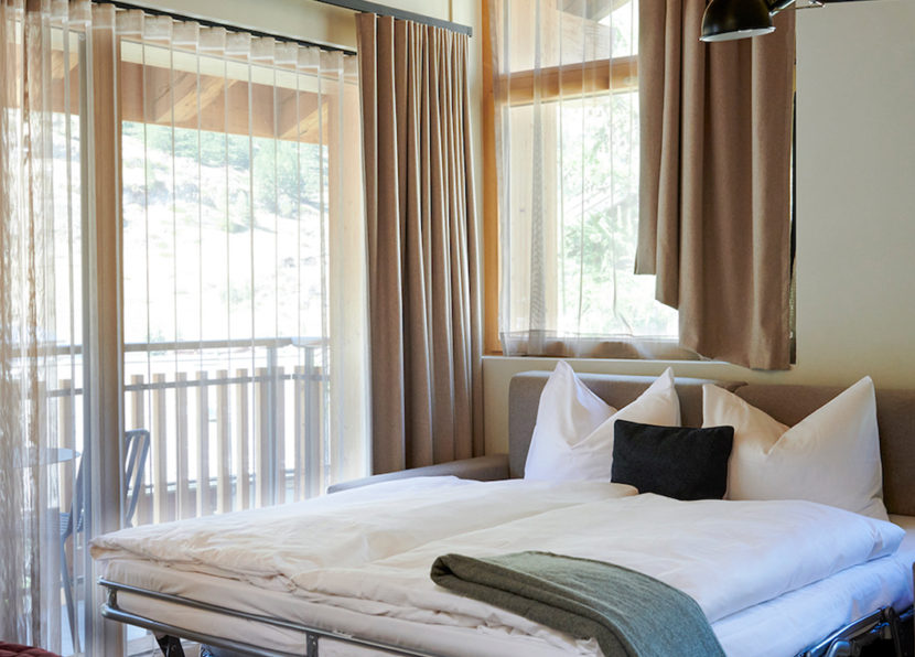 Schlafbereich des Penthouse Matterhorn im Hotel Carina Zermatt mit Bett und Balkonzugang