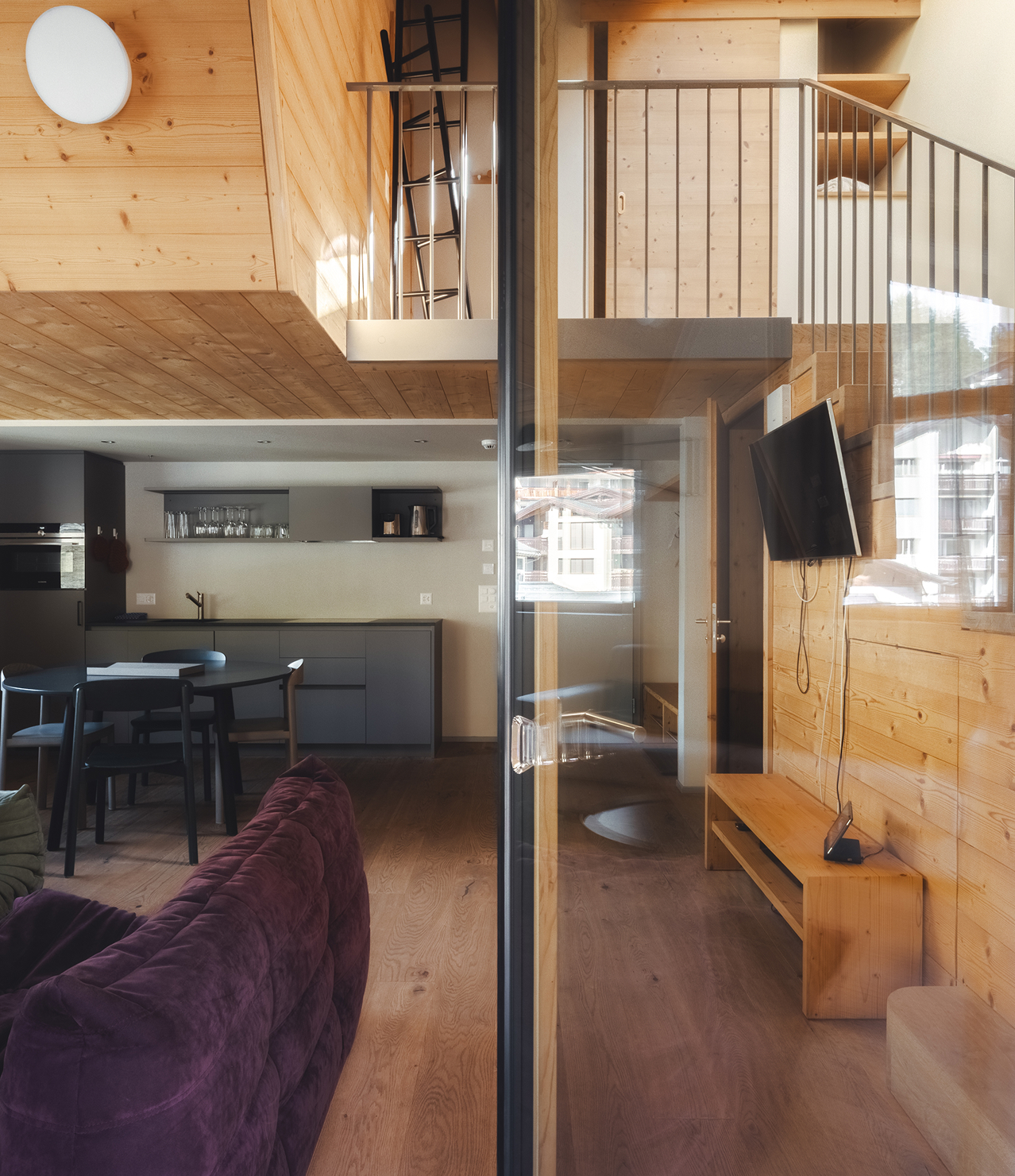 Wohn- und Küchenbereich des Penthouse Matterhorn im Hotel Carina Zermatt, teilweise als Spiegelung in einer Glastür sichtbar