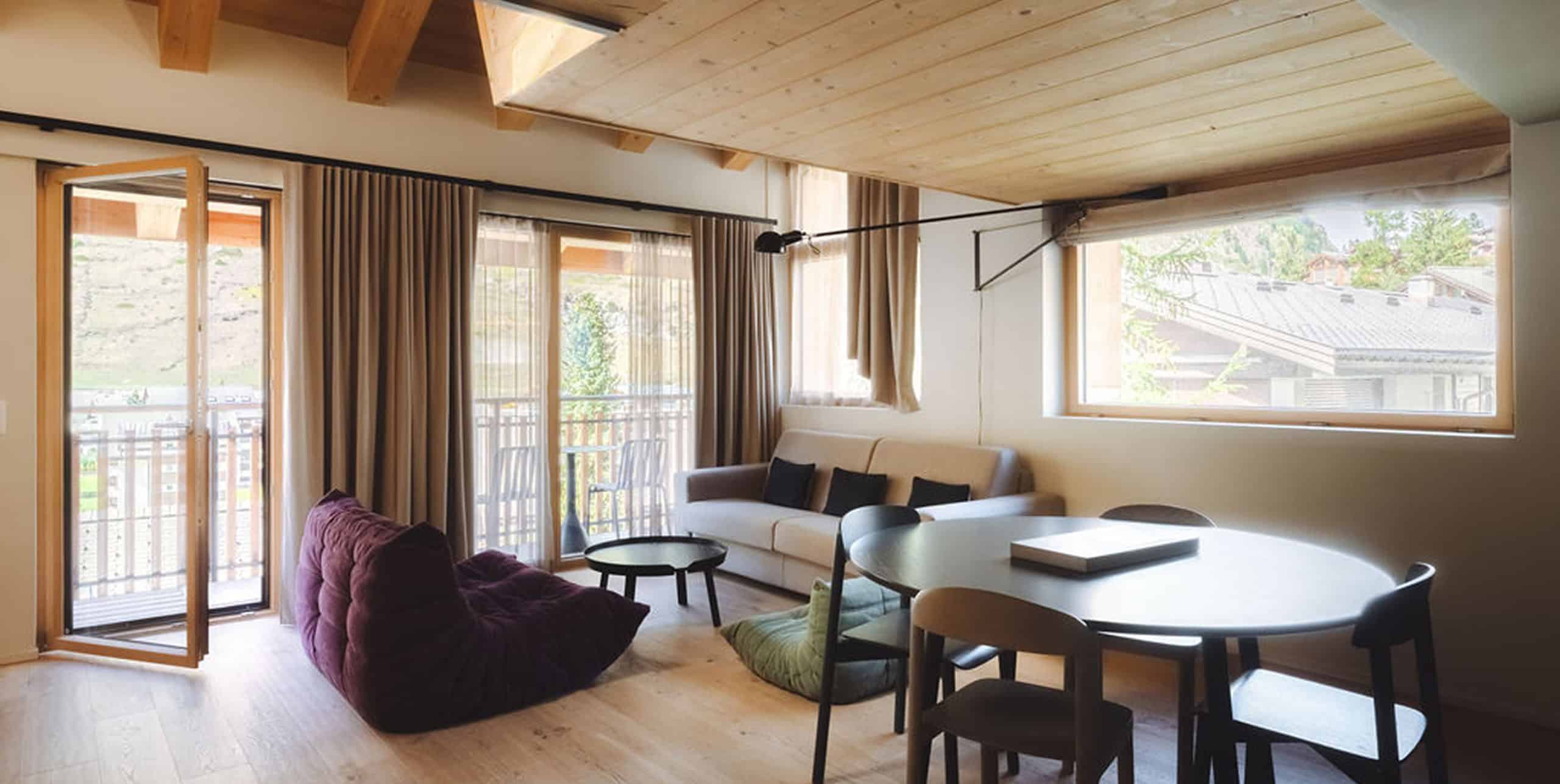 Wohn- und Essbereich eines Zimmers im Hotel Carina Zermatt mit Sofa, Esstisch und Balkonzugang