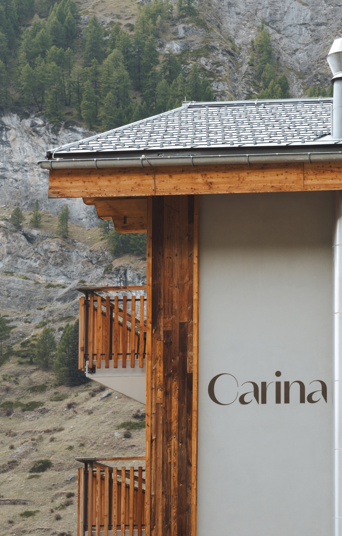 Außenansicht des Hotel Carina Zermatt mit Holzfassade und Balkonen; im Hintergrund ein felsiger Berghang