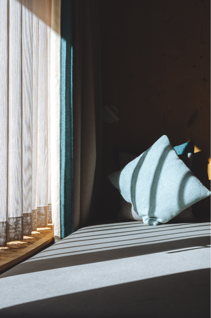 Lumière naturelle sur les coussins et le linge de lit dans une chambre de l’Hôtel Carina Zermatt