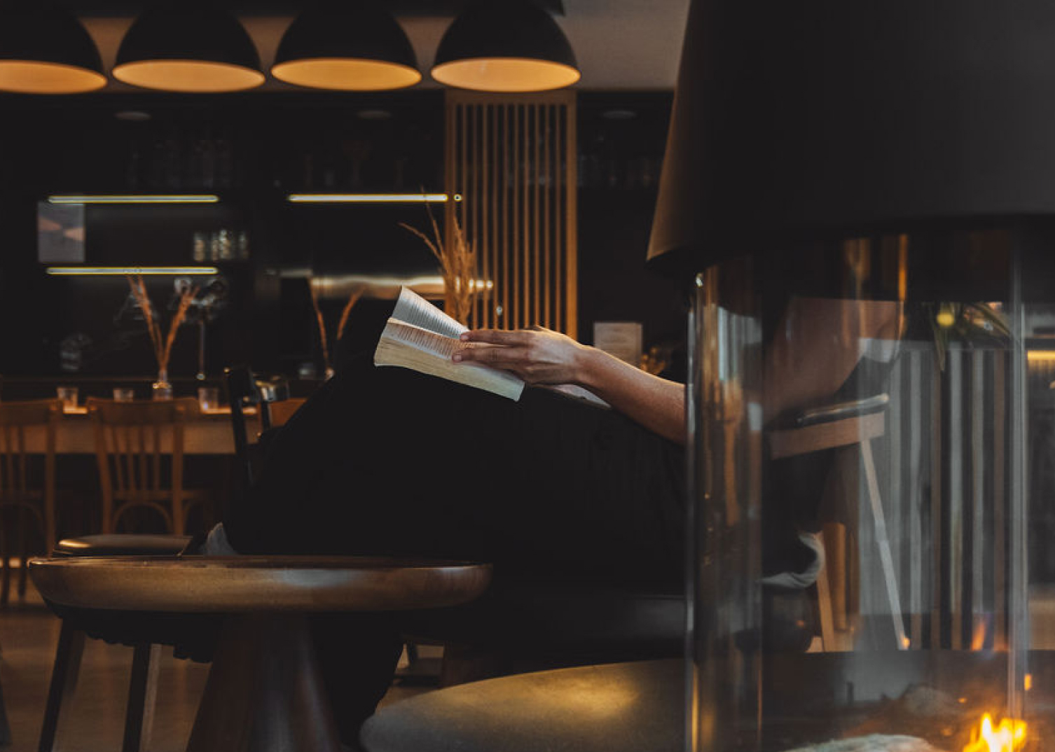 Personne se détendant dans le lounge en lisant un livre près d’une cheminée.