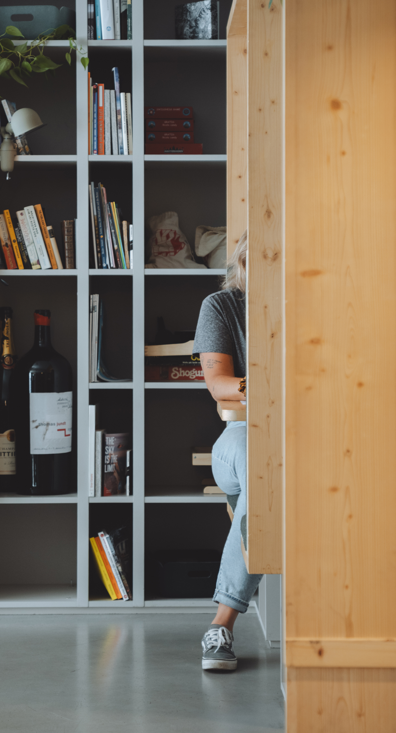 Personne partiellement visible derrière une cloison en bois dans un espace commun avec bibliothèque en arrière-plan.