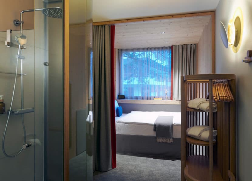 View from the bathroom into the double room with shower and sleeping area at Hotel Carina Zermatt.