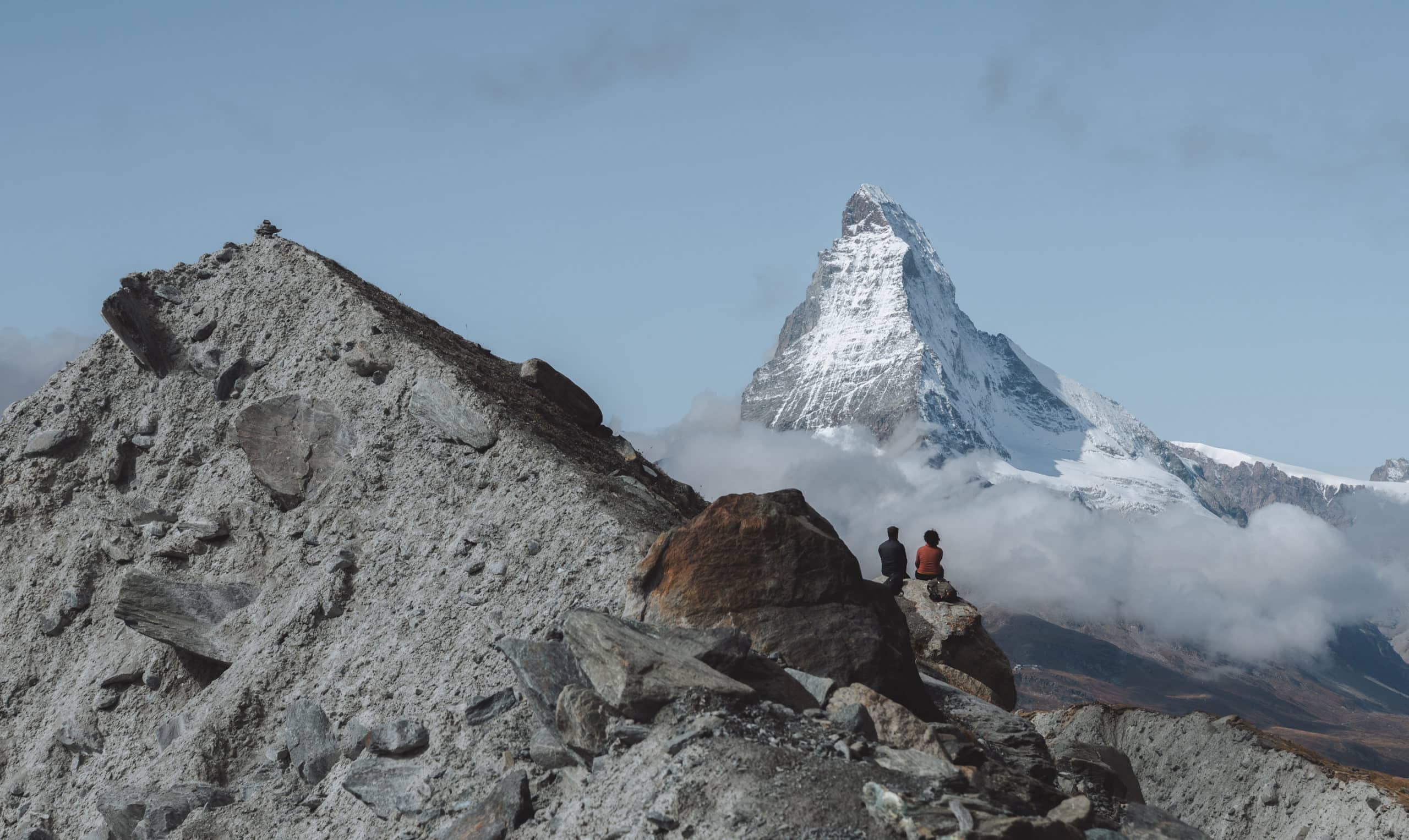 Zwei Menschen sitzen auf Felsen und blicken auf das Matterhorn in der Zermatter Bergwelt.