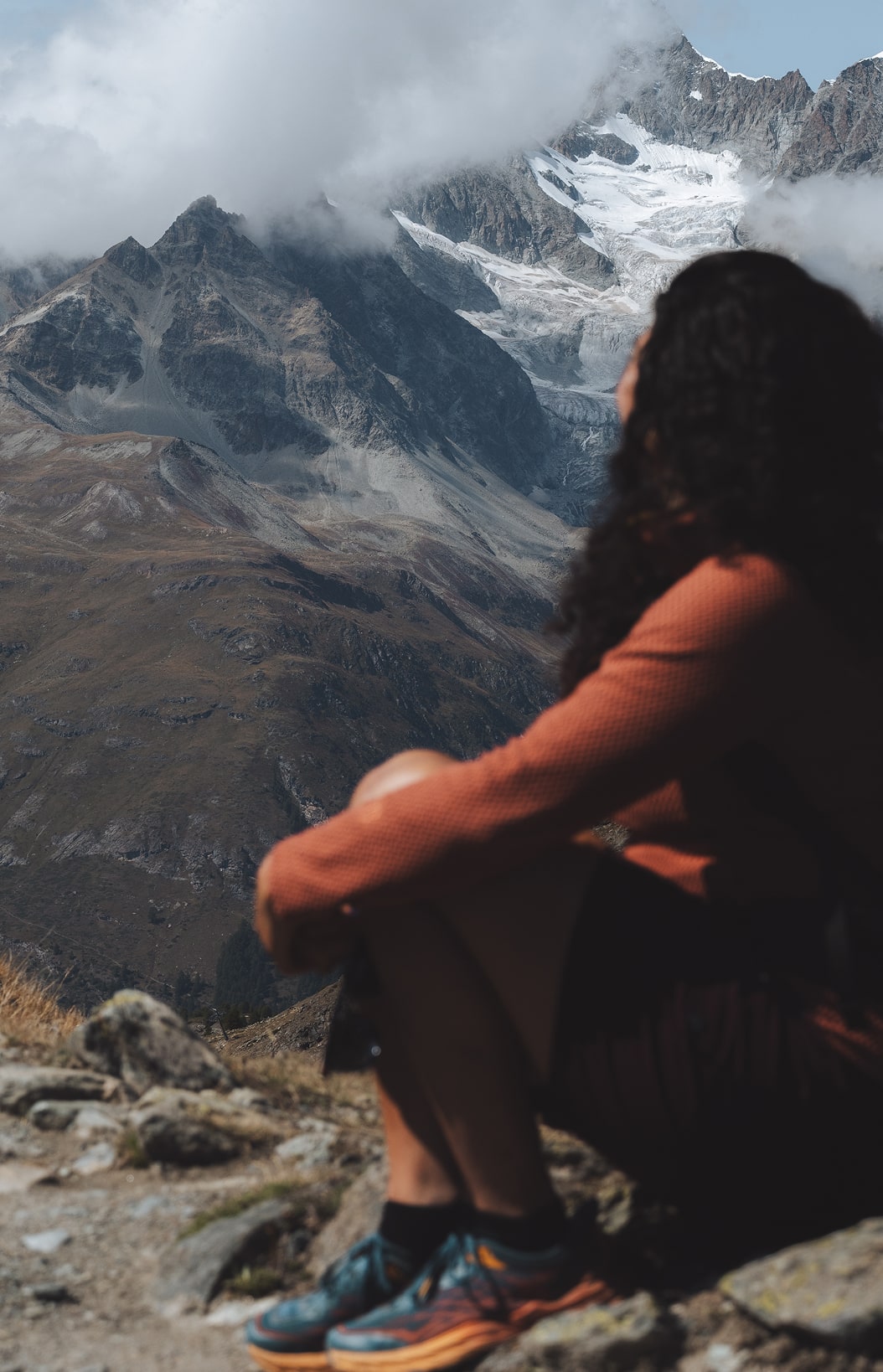 Person sitzt auf einem Felsen und blickt still auf die alpine Berglandschaft.