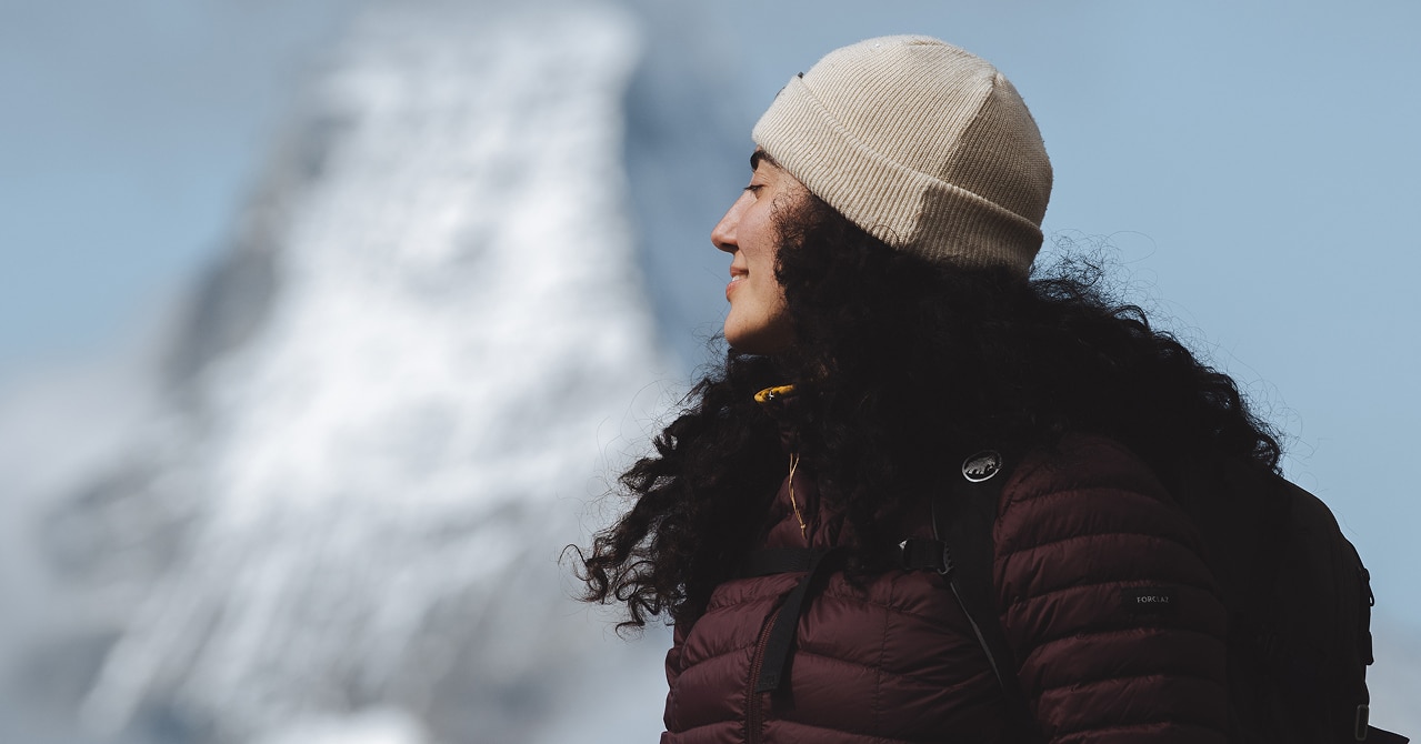 Frau in Winterkleidung blickt auf das verschneite Matterhorn bei klarem Himmel.