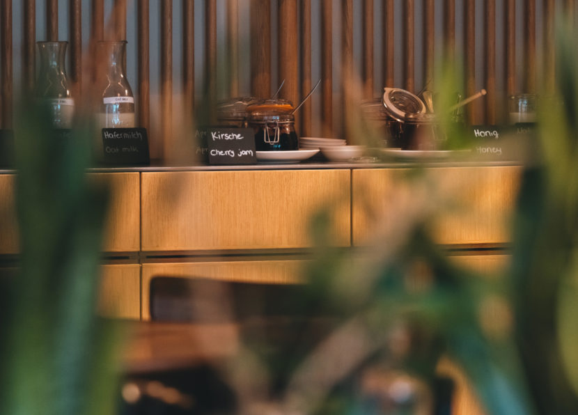 Frühstücksbuffet mit beschrifteten Gläsern Marmelade und Honig auf einem Holztresen.