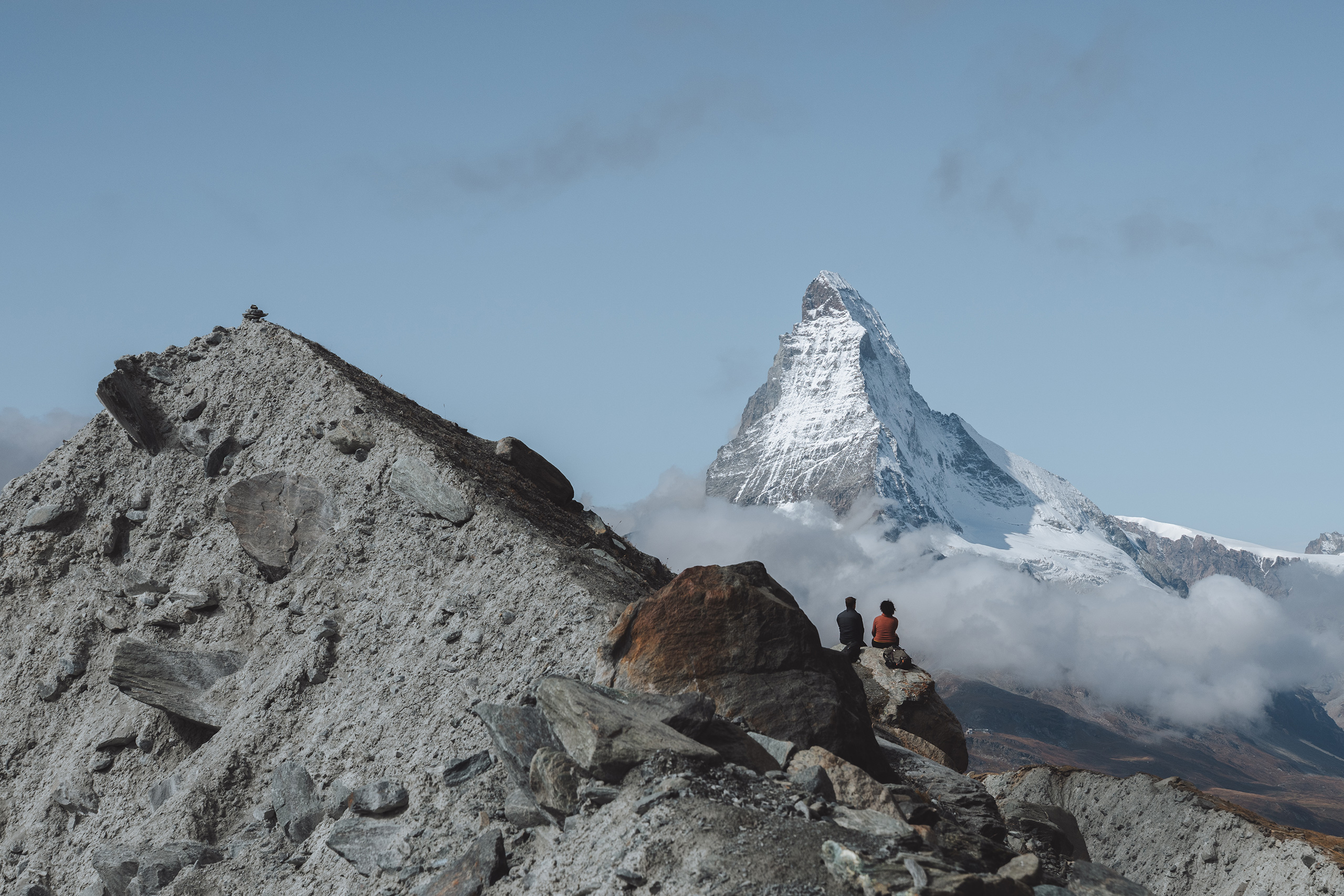 Zwei Personen sitzen auf Felsen und blicken auf das Matterhorn in einer alpinen Berglandschaft