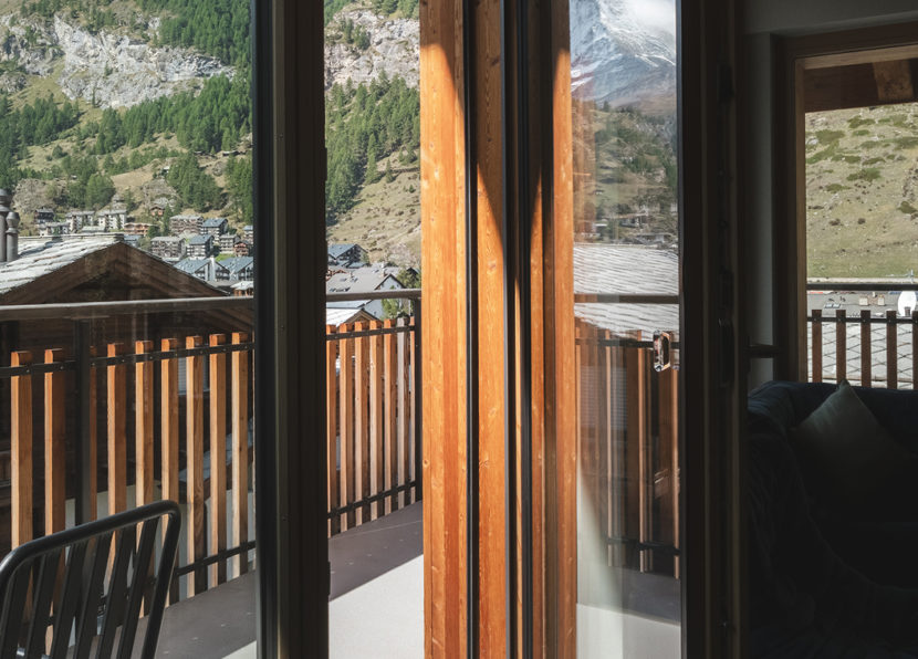 Blick vom Penthouse Matterhorn im Hotel Carina Zermatt durch die Balkontür auf Dorf und Berge
