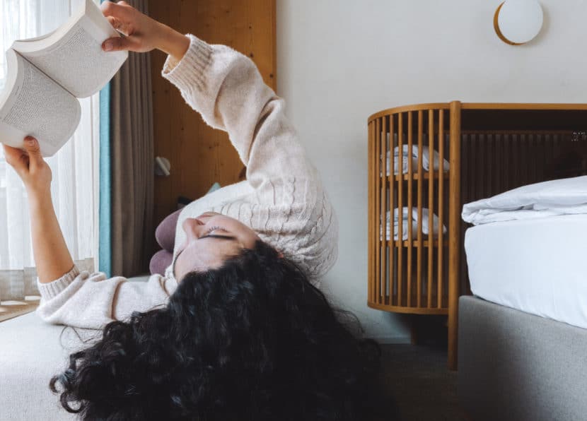 Frau liest entspannt am Fenster im Matterhorn Zimmer des Hotel Carina Zermatt mit warmem Holzinterieur und Tageslicht.