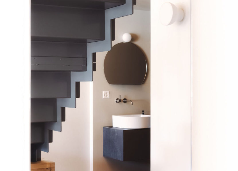 Vue détaillée de la salle de bain avec lavabo et miroir sous l’escalier.