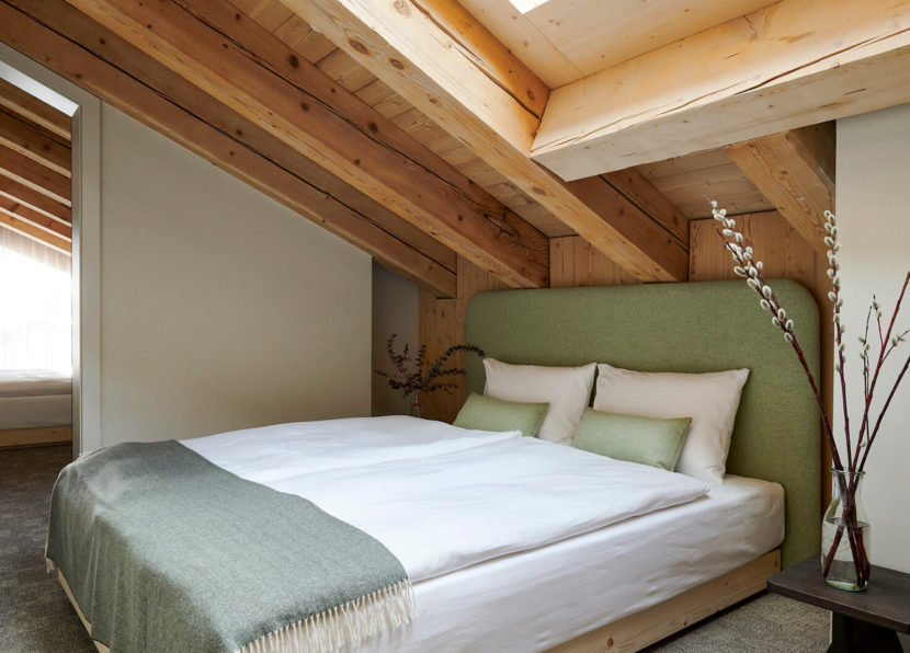 Chambre chaleureuse avec plafond en bois, lit double et tête de lit verte.