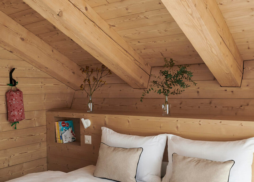Espace nuit sous toit en bois avec lit double et plantes décoratives.