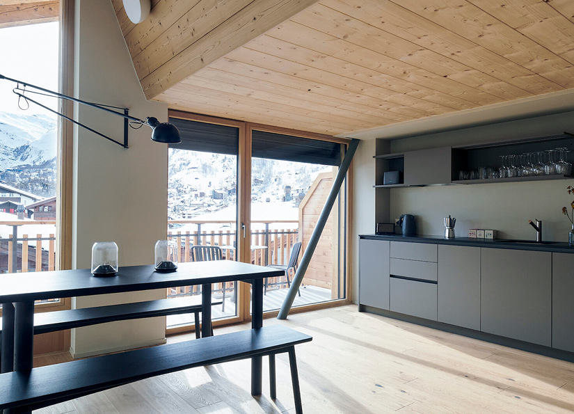 Cuisine ouverte avec coin repas et grandes baies vitrées donnant accès au balcon avec vue sur les montagnes.