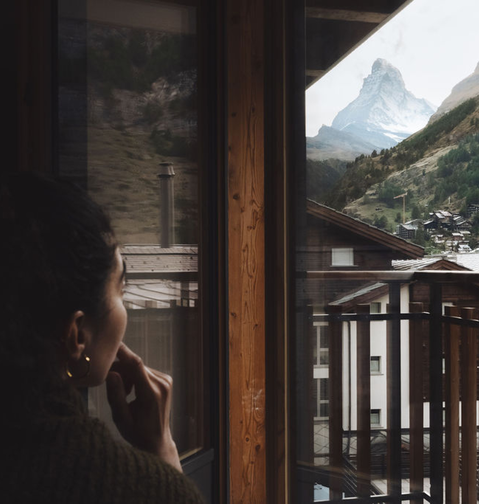 Person blickt vom Zimmer durch eine Glastür auf den Balkon; draußen ist das Matterhorn sichtbar, teilweise als Spiegelung im Glas