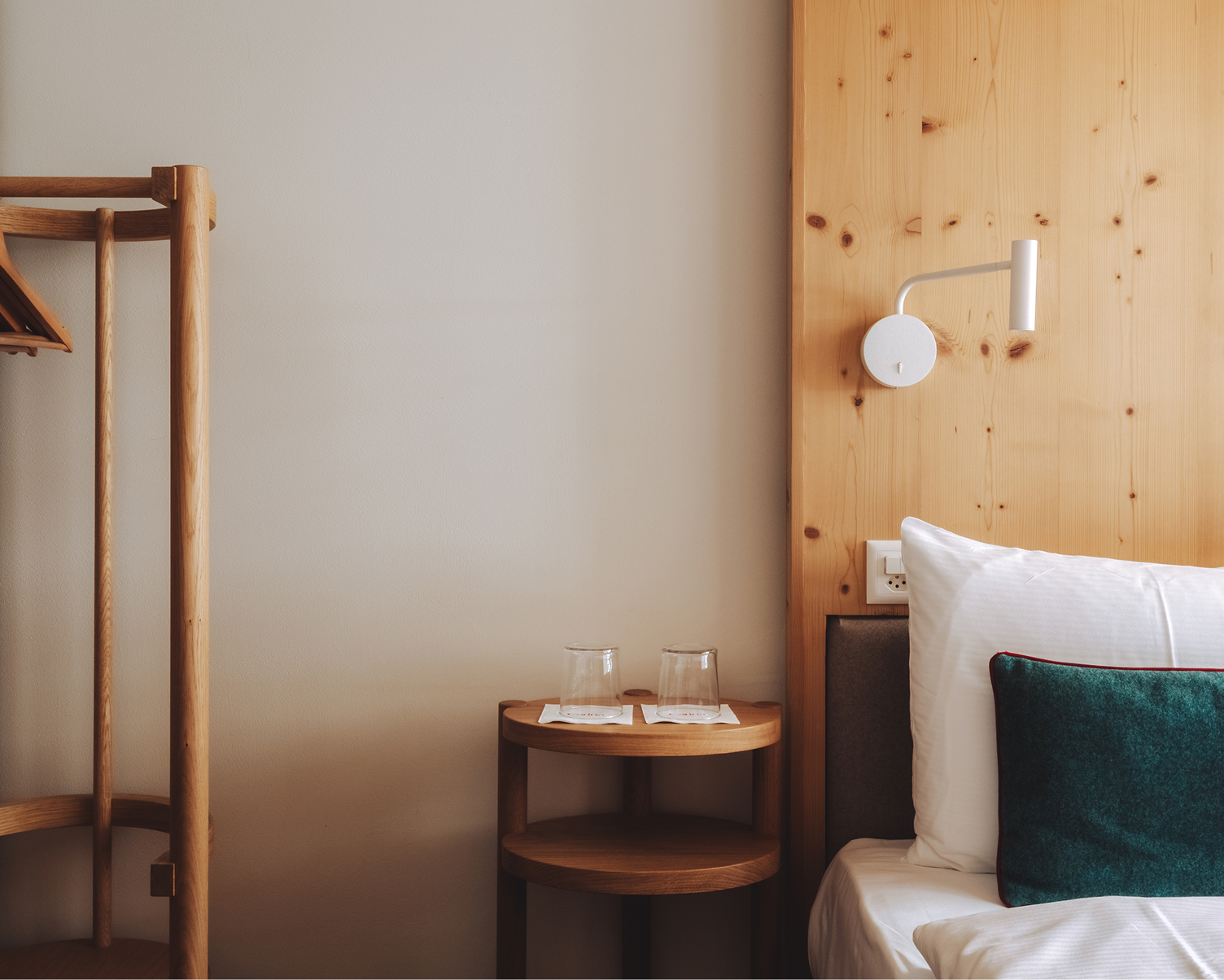 Détail du lit avec table de chevet, lampe et mur en bois dans une chambre de l’Hôtel Carina Zermatt