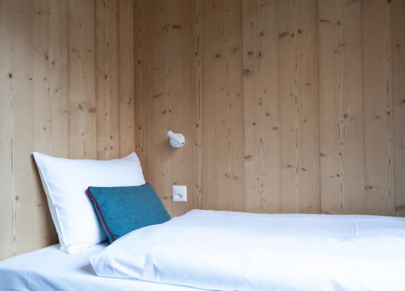 Lit simple dans la chambre twin avec intérieur en bois alpin à l’Hôtel Carina Zermatt.